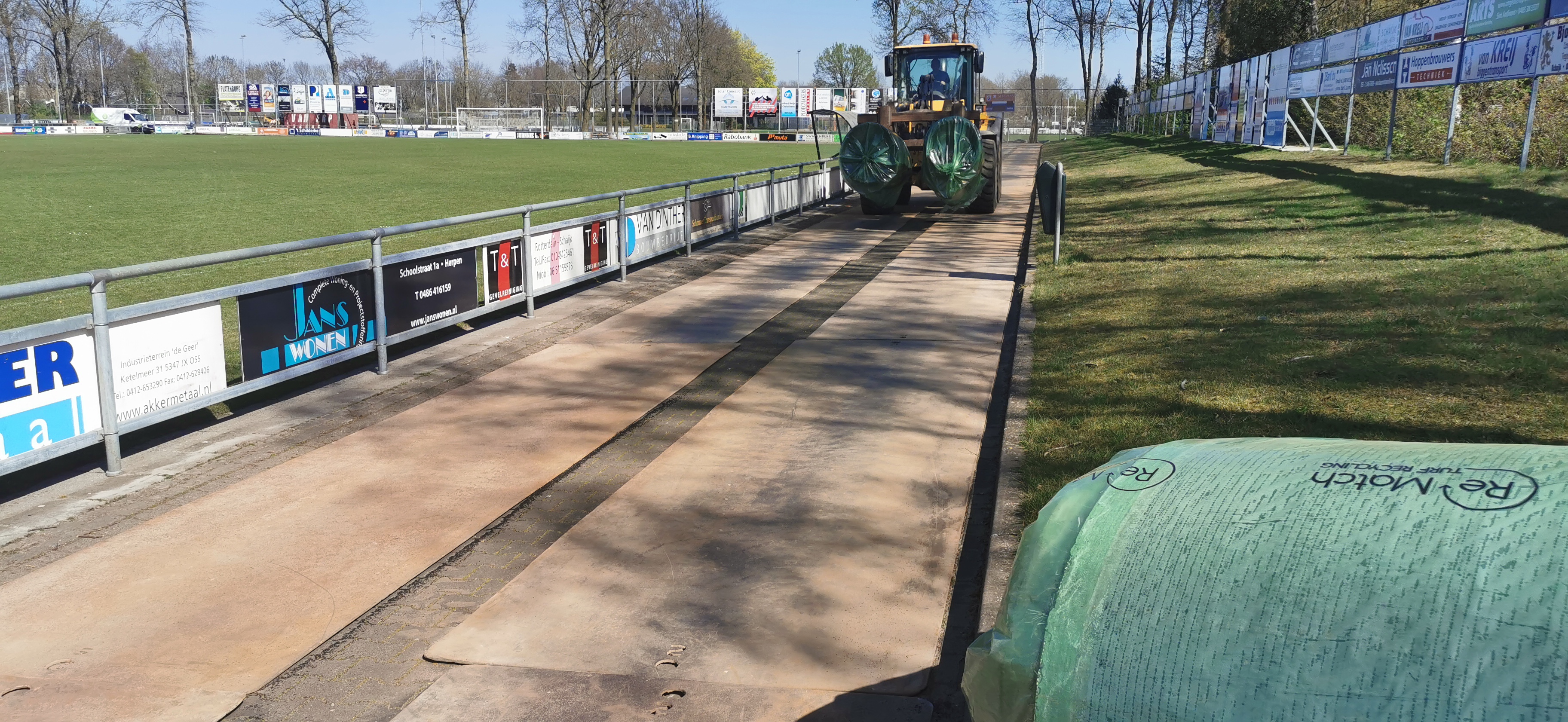 Oud kunstgras wordt door shovel afgevoerd over rijplaten